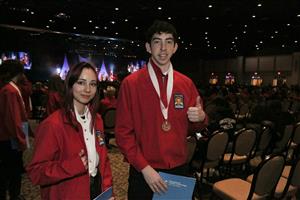 Two Multimedia students in red jackets with thumbs-up and bronze medals